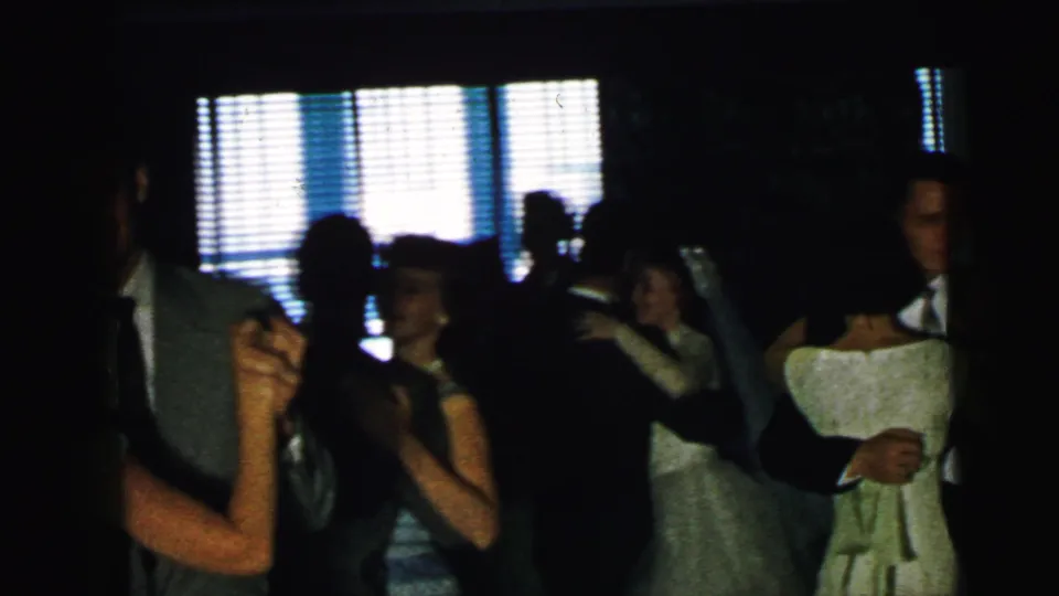 1964 Camden home-movie frame with dancing guests silhouetted against bright venetian blinds during a formal party.