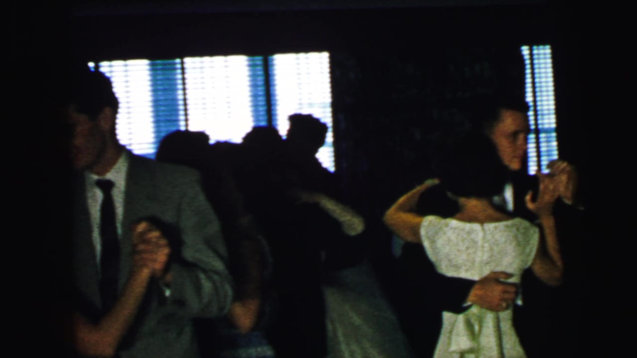 Couples dancing in a dim room with bright window blinds behind them.