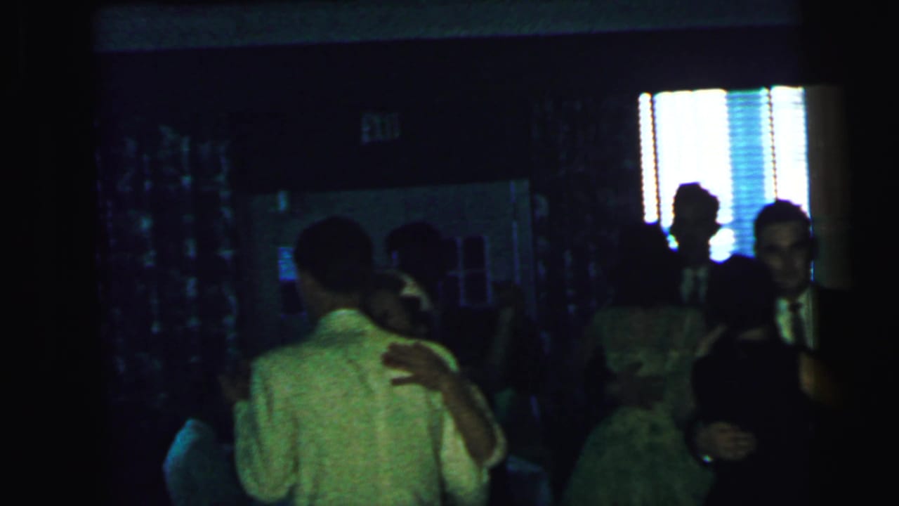 1964 Camden event footage with couples dancing under low light, framed by a bright window, curtains, and seated guests.