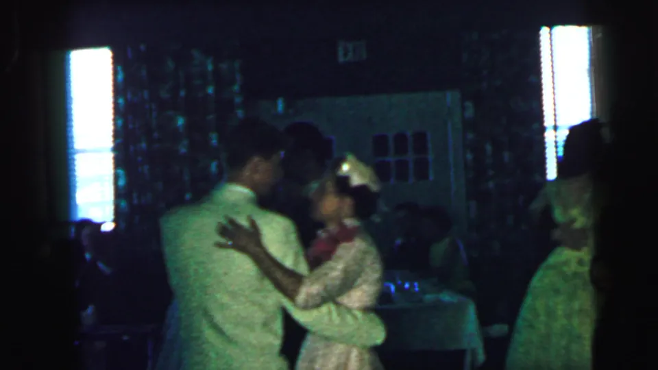 A man in a light suit dances with a woman in a pale dress during a 1964 Camden indoor event, with window blinds behind them.