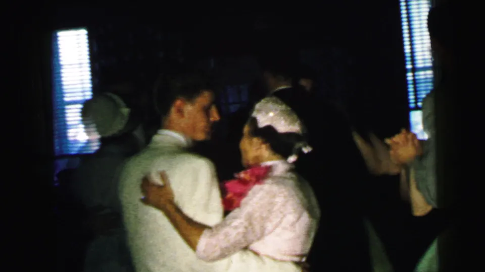 At the 1964 Camden reception, guests dance in pairs, including a woman in pink and suited men under window light.
