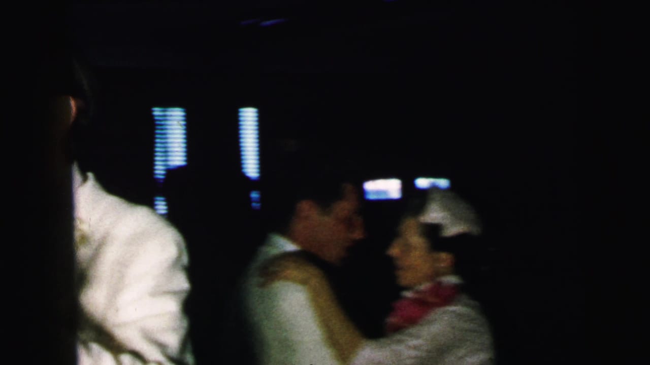 Several guests dance in a dark interior, with a couple visible near the right side.
