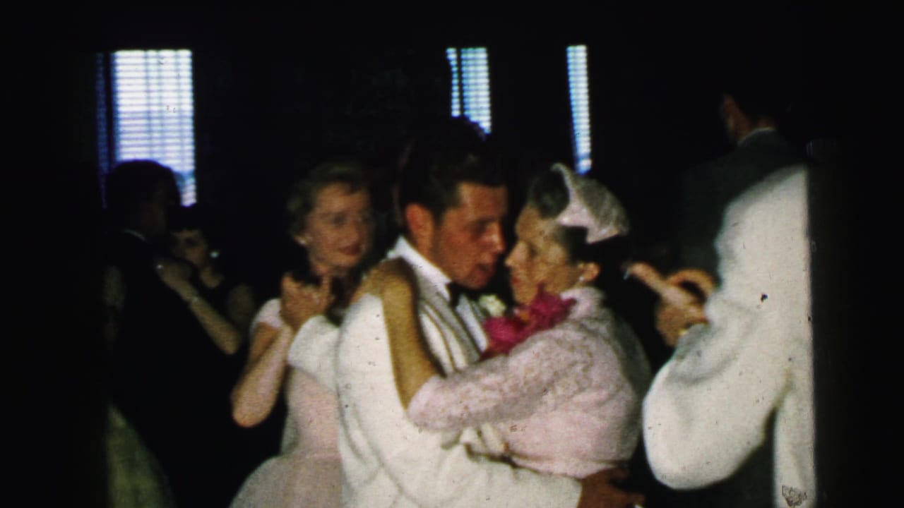 Couple dancing closely at a dim wedding reception with guests nearby.