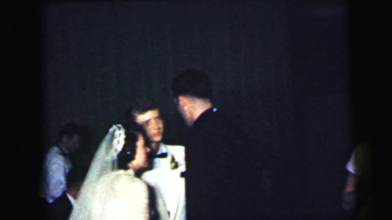 The bride and groom appear in conversation with a dark-suited guest during the 1964 Camden, New Jersey wedding reception.