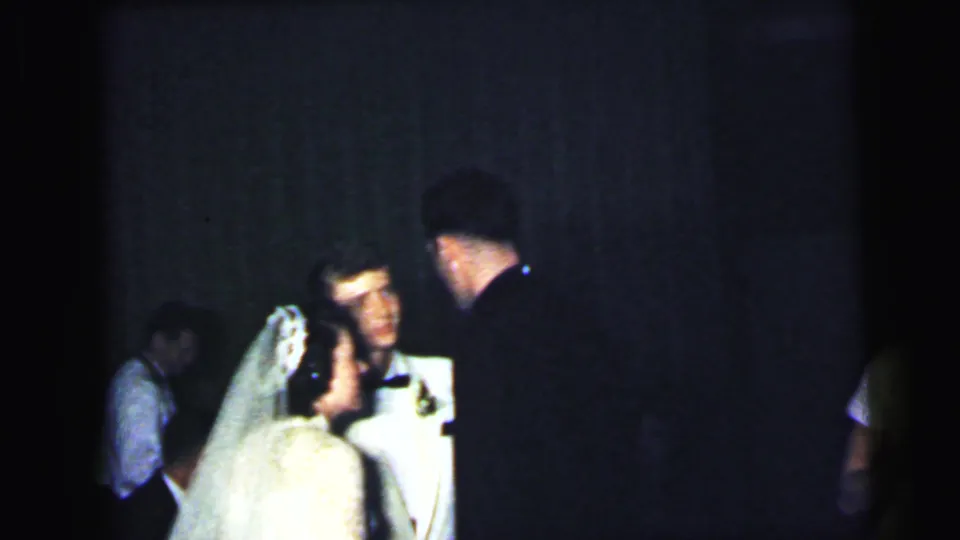 The bride and groom appear in conversation with a dark-suited guest during the 1964 Camden, New Jersey wedding reception.