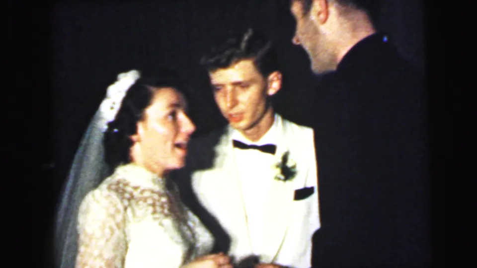 Close view of the bride, groom in a white dinner jacket, and dark-suited guest during a Camden wedding reception conversation in 1964.