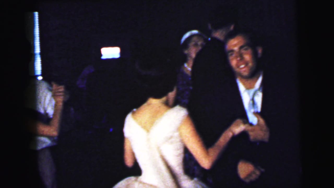 Couple dancing in a dim room while other party guests stand nearby.