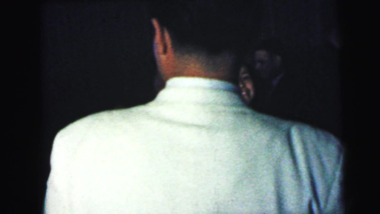 Back of a man in a light shirt beside a partially visible woman in a dark room.