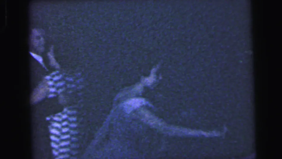 Blue-tinted 8mm frame from the Camden party, showing guests dancing in low light with a striped dress and blurred movement.
