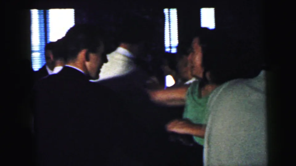 Camden, New Jersey home-movie frame from 1964 showing adults dancing in a dim interior, including a suited man and guests in light shirts.