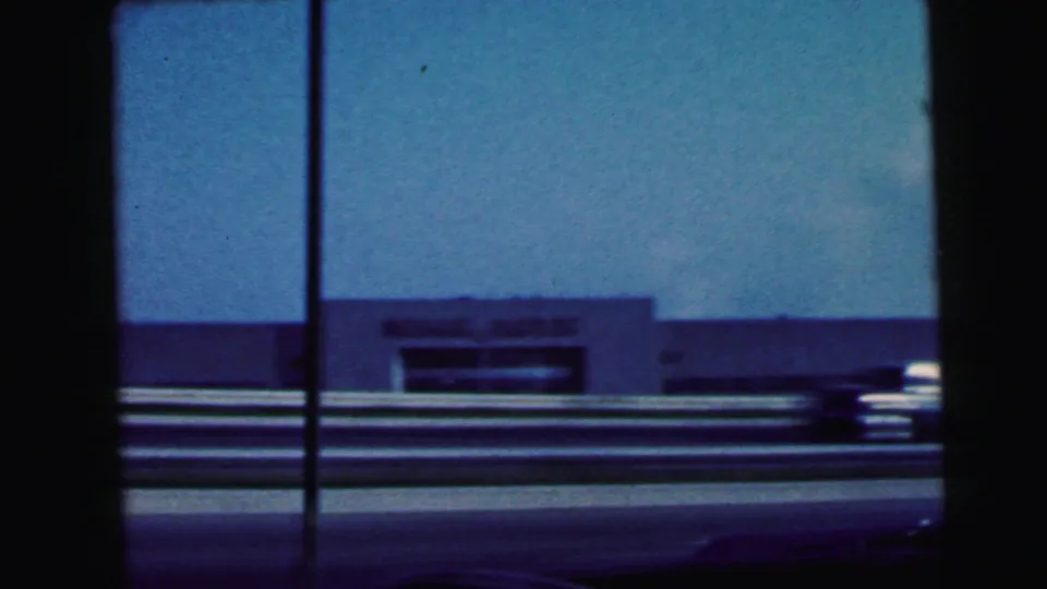 1964 passenger-window view near Camden, New Jersey, with a roadside building, guardrails, and blue-tinted sky passing by.