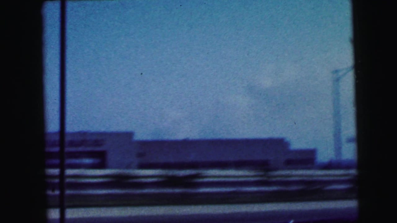 View through a car window toward low roadside buildings under a blue sky.