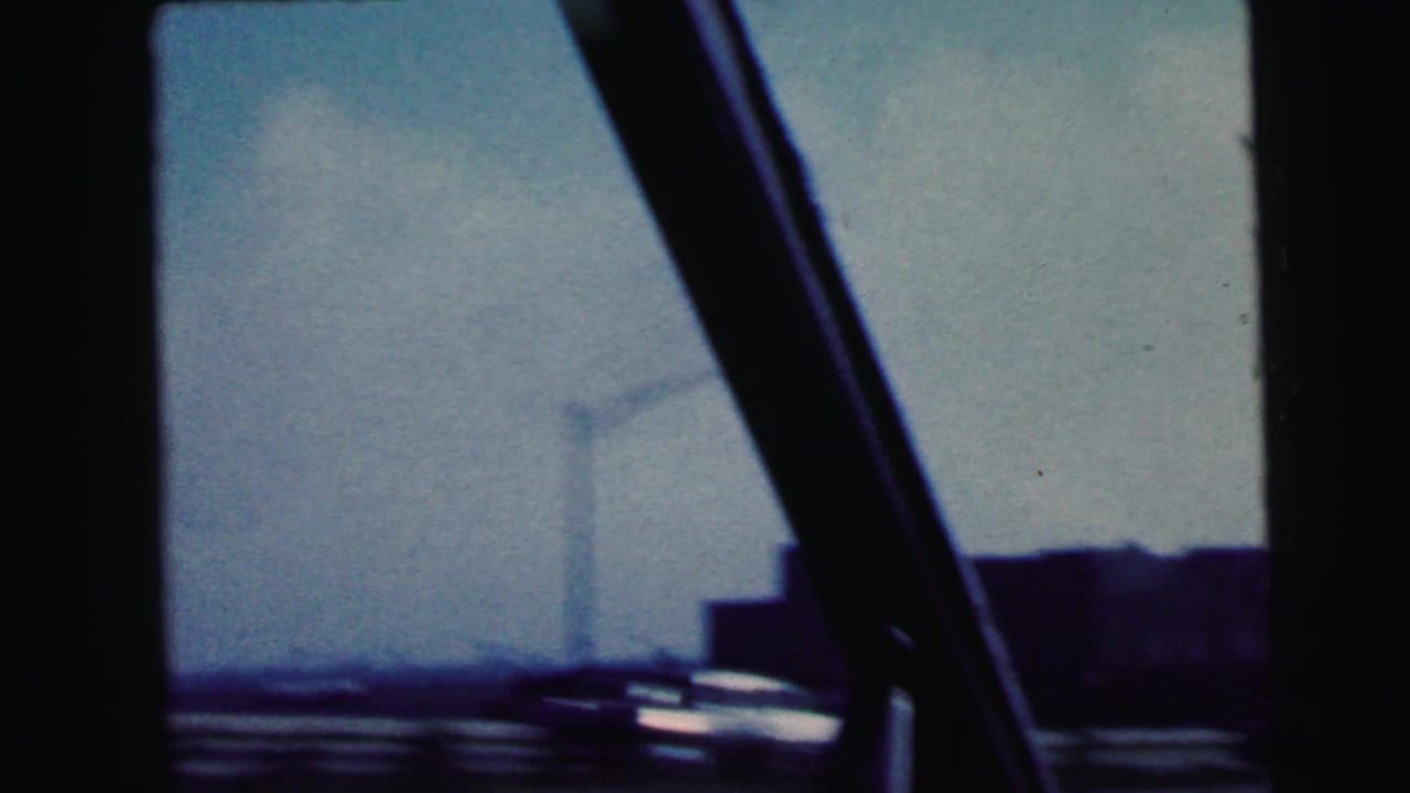 Blurred roadside view through a vehicle window with a passing car and distant buildings.