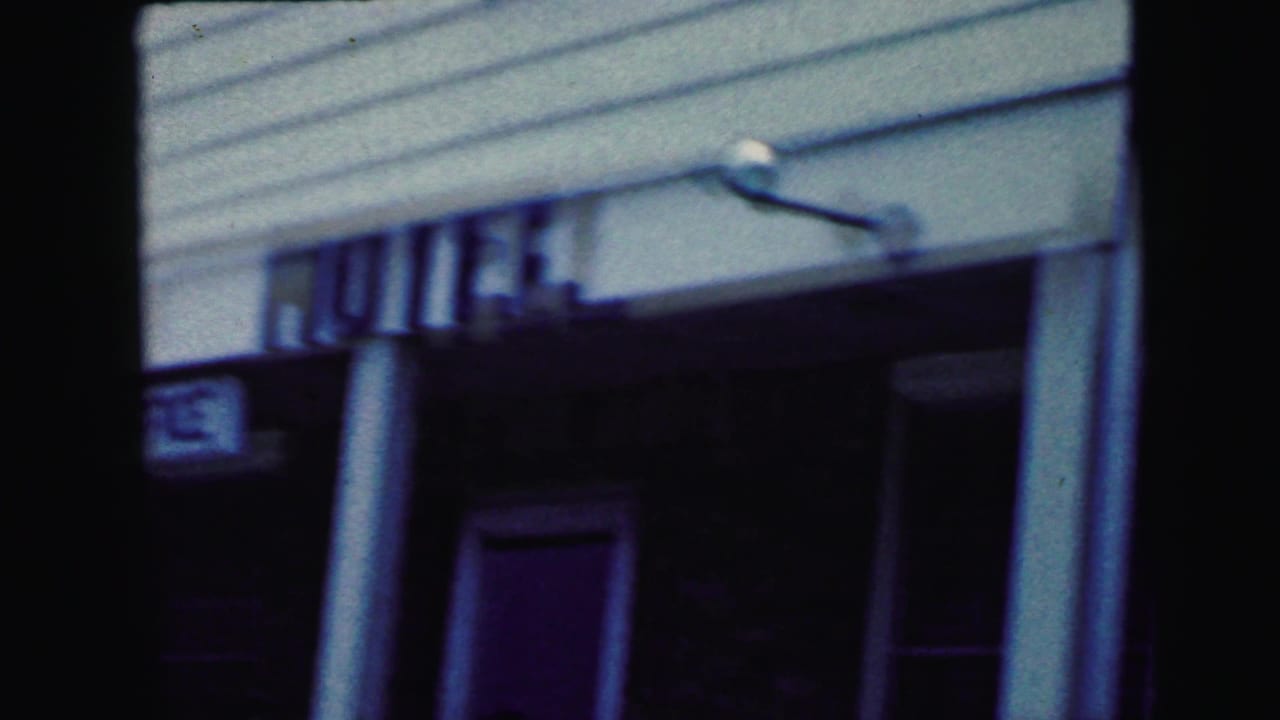 Exterior of the Fountain Hotel or Motel entrance with white siding, columns, and partially legible signage in the Camden 1964 footage.