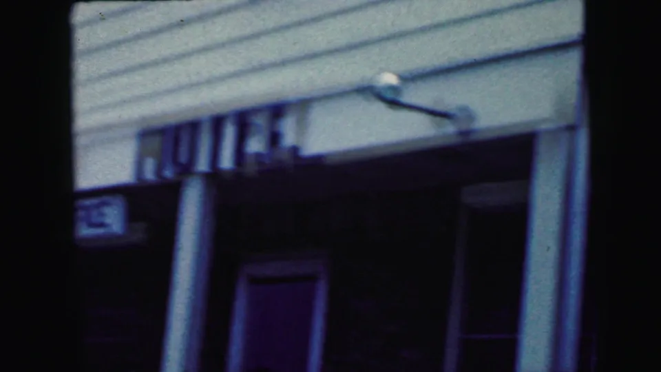 Exterior of the Fountain Hotel or Motel entrance with white siding, columns, and partially legible signage in the Camden 1964 footage.