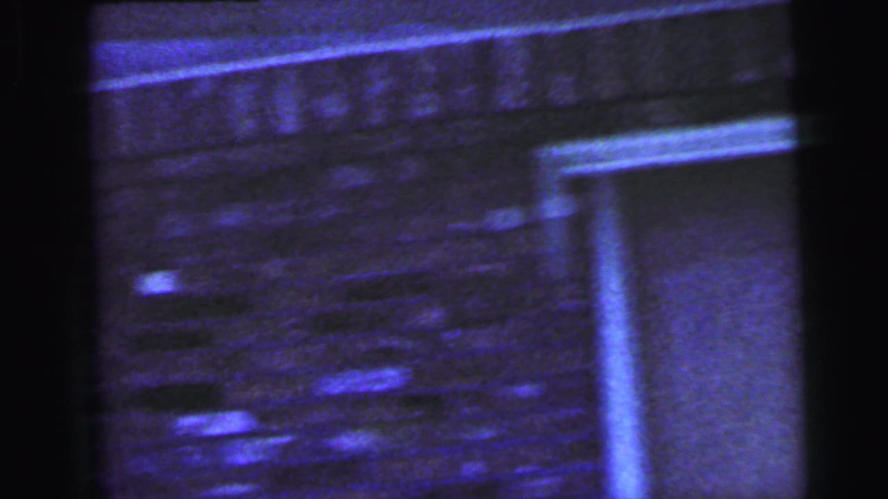 Soft, blue-shifted 1964 Camden frame showing a brick exterior wall, doorway, and heavy 8mm film edges.