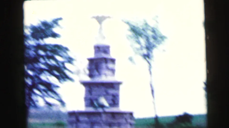 Overexposed 1964 Camden frame showing a tiered stone monument or fountain form near trees and open grass.