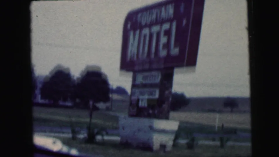 1964 Camden, New Jersey 8mm frame showing a purple Fountain Motel sign along a roadside, viewed through a moving vehicle.