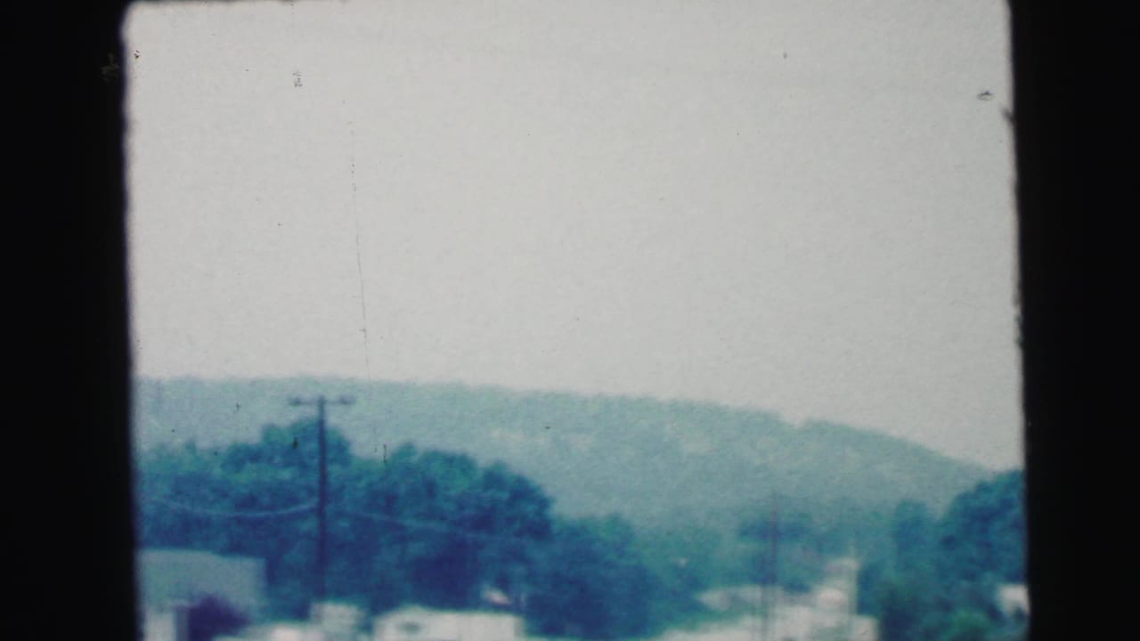Camden, New Jersey roadside view from 1964 8mm footage with utility poles, trees and low wooded hills in the distance.