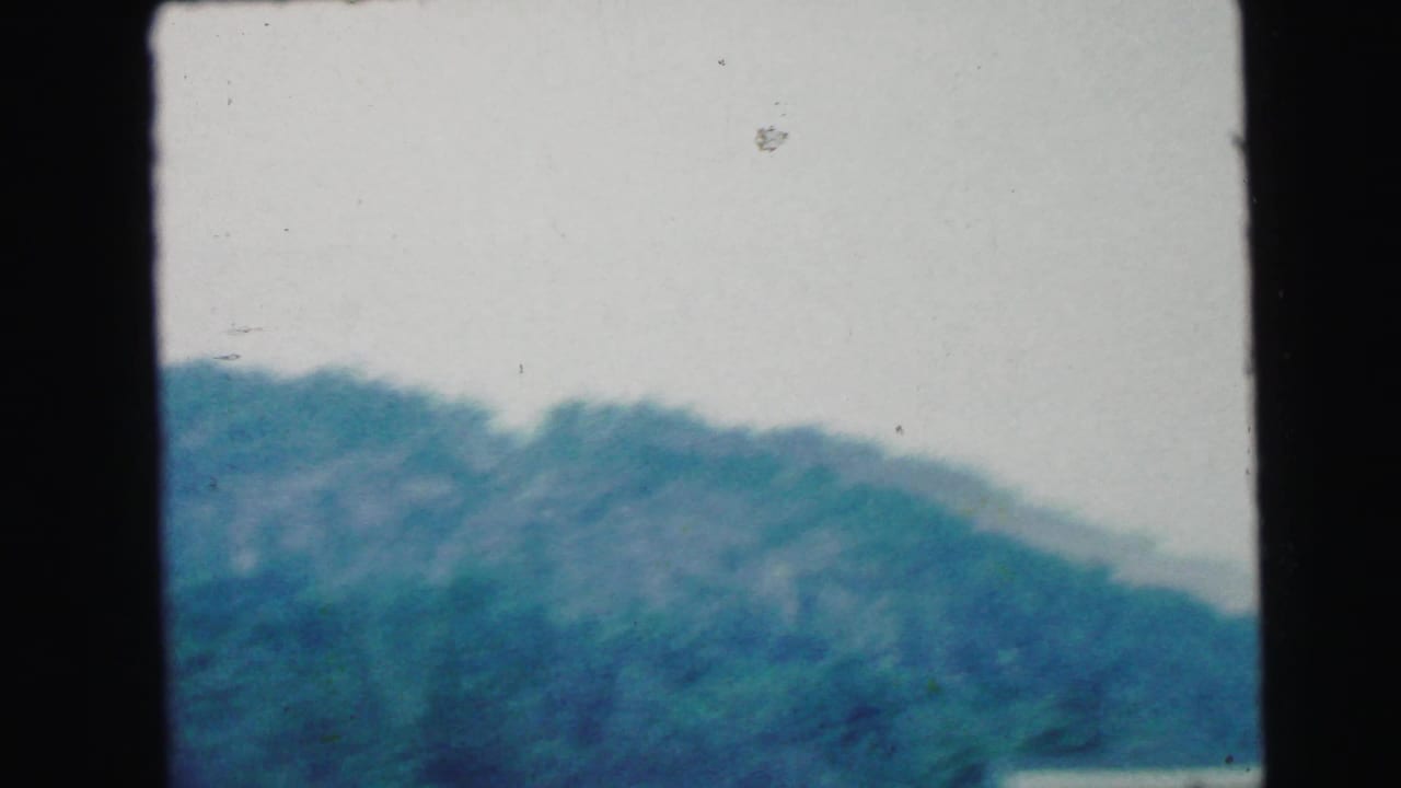 1964 8mm home-movie frame showing hazy wooded hills in rural New Jersey, with soft focus and dark frame borders.