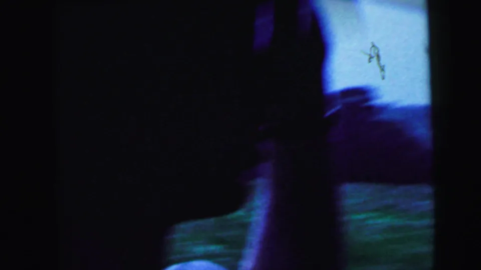 Blurred 8mm frame from the moving car, with dark foreground obstruction, blue sky, green roadside, and motion smear.