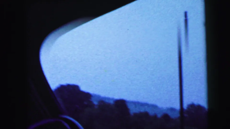 End frame from a 1964 8mm driving shot, looking through a car window toward hills, sky, and a roadside utility pole.
