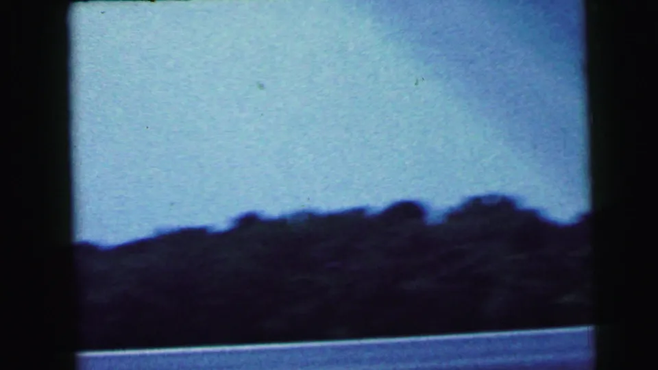 8mm home movie still from 1964 showing a silhouetted treeline against a pale blue sky, likely filmed from a moving vehicle in New Jersey.