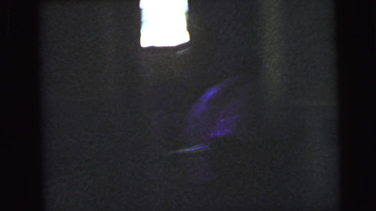 Very dark interior with a bright overexposed rectangular light source at upper centre and a dark purple mass below, possibly a figure.
