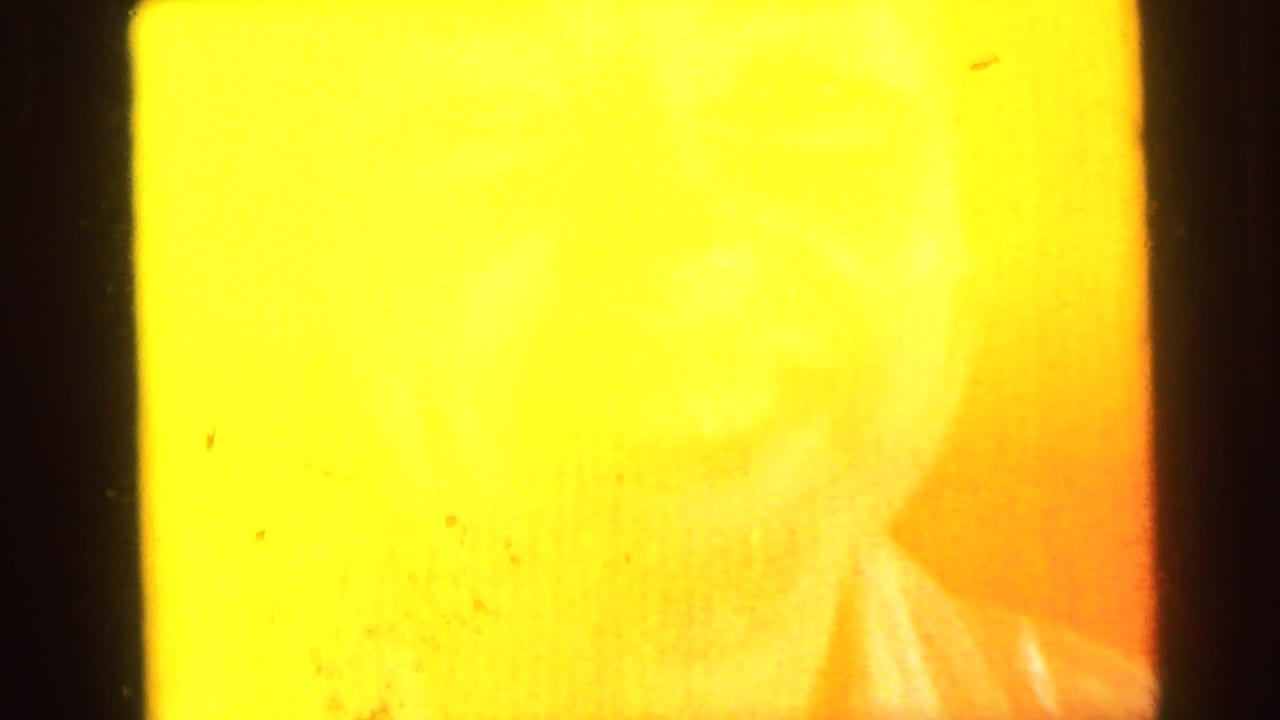 Heavily overexposed 8mm frame; faint impression of a woman's face visible through yellow light wash.