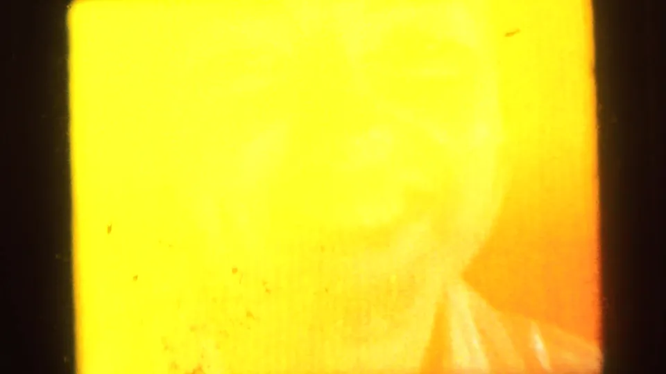 Opening frame of a 1964 Camden, New Jersey home movie; extreme overexposure leaves only a faint female face visible through a yellow-orange wash.