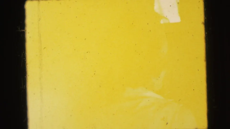 Transitional overexposed frame from a 1964 8mm home movie showing near-complete yellow flare with a faint partial form at top right.