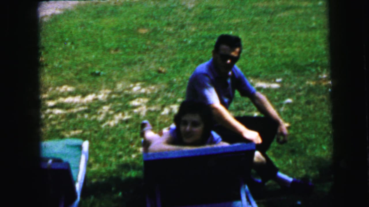 Man in blue shirt and a woman in a blue container on a suburban lawn, likely Camden, New Jersey, circa 1964 8mm home movie.