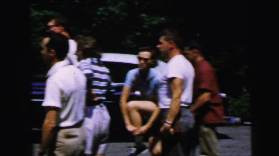 Five or six young adults in 1960s summer attire — white t-shirts, shorts, striped shirt, sunglasses — standing in a tree-shaded outdoor area, Camden area, New Jersey, circa 1964.