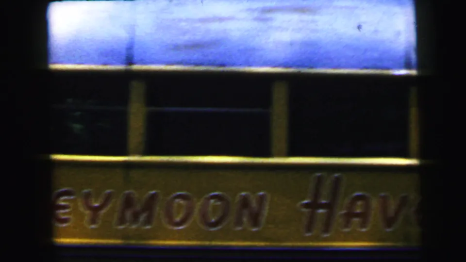 Partial 'Honeymoon Haven' sign with gold embossed lettering, framed by darkness, from 8mm home movie footage attributed to Camden, New Jersey, c. 1964.