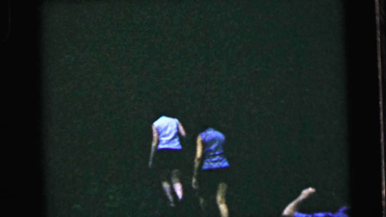 Two women in mid-1960s summer clothing walking away from camera across a grassy lawn; 8mm home movie, United States, circa 1964.