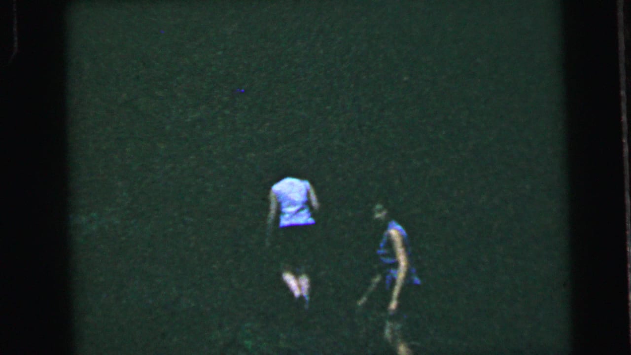 Two women walking on a dark green lawn, smaller in frame, seen from behind or at distance.