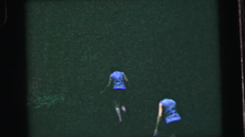 Two women at different positions on a grassy slope, one lower or leaning forward; 8mm home movie, United States, circa 1964.