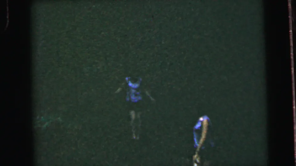 Two female runners in blue sleeveless tops and dark shorts race across an open field, possibly Camden, New Jersey, circa 1964; heavy grain and greenish cast from 8mm film.