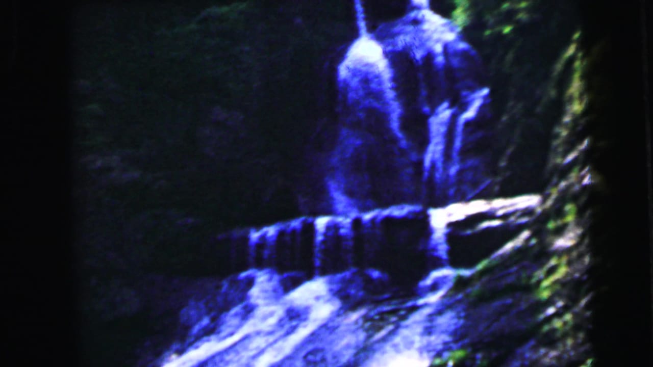 Blue-tinted 8mm frame of a multi-tier waterfall cascading over dark rocky cliffs with heavy vignetting.