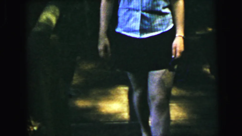 Figure in shorts and blue-striped shirt descending stone steps in a dark shaded setting; 8mm home-movie footage, Camden, New Jersey, circa 1964.