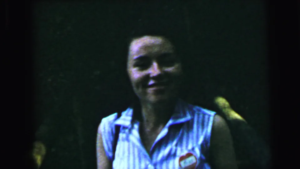 Close-up of a smiling young woman in a blue-and-white striped sleeveless uniform with a small chest badge; 1964 8mm home-movie footage, Camden, New Jersey area.