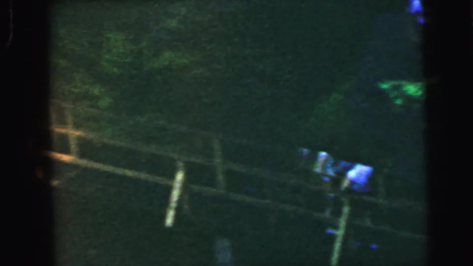 End-of-clip 8mm frame with severe underexposure and green color shift; faint bridge railing and a small figure visible, consistent with a 1964 park setting.