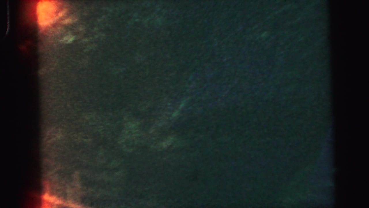 Dark green field with red-orange light leak at left edge; waterfall not yet in frame.