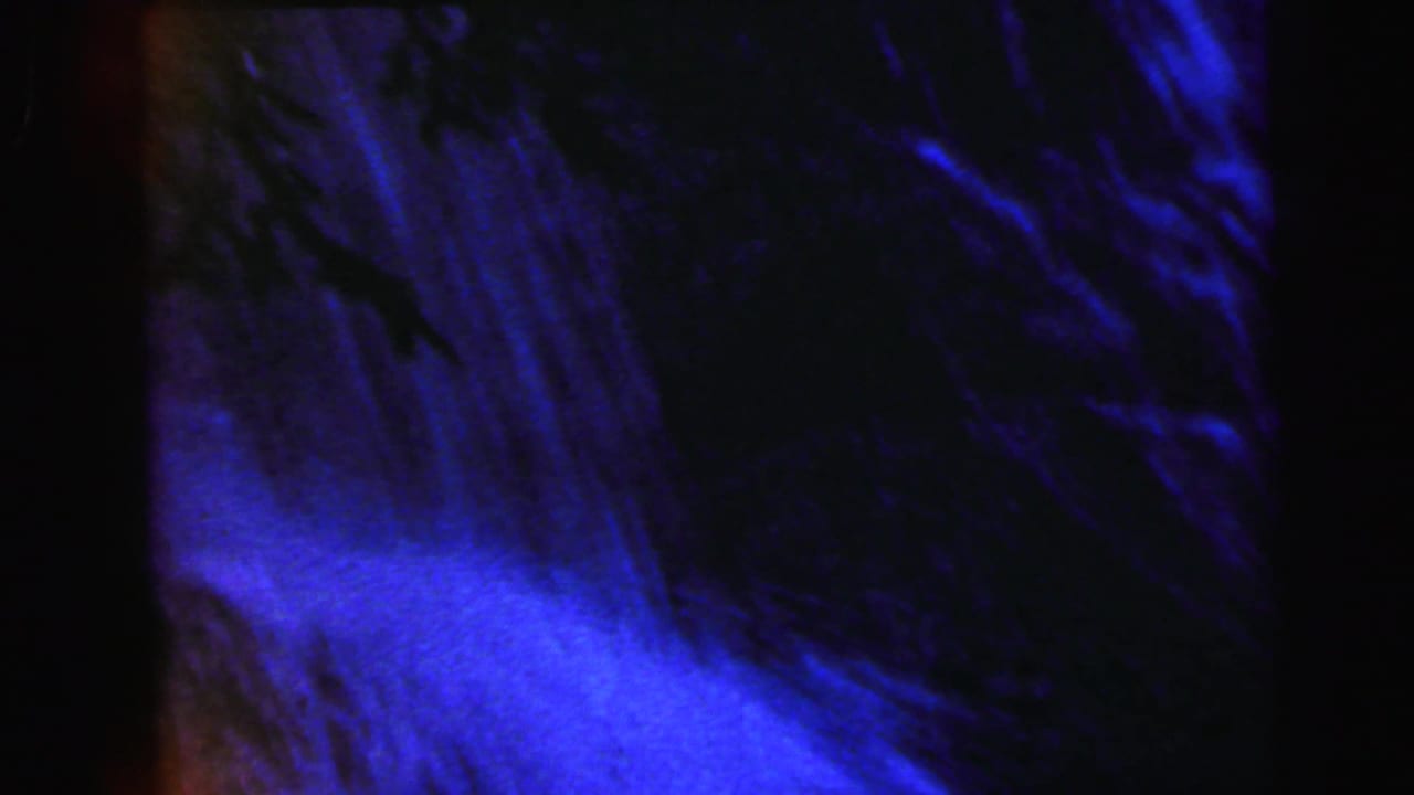 Mid-pan 8mm frame from 1964 showing a waterfall close-up with heavy blue-purple dye shift and streaking white water against a dark backdrop.