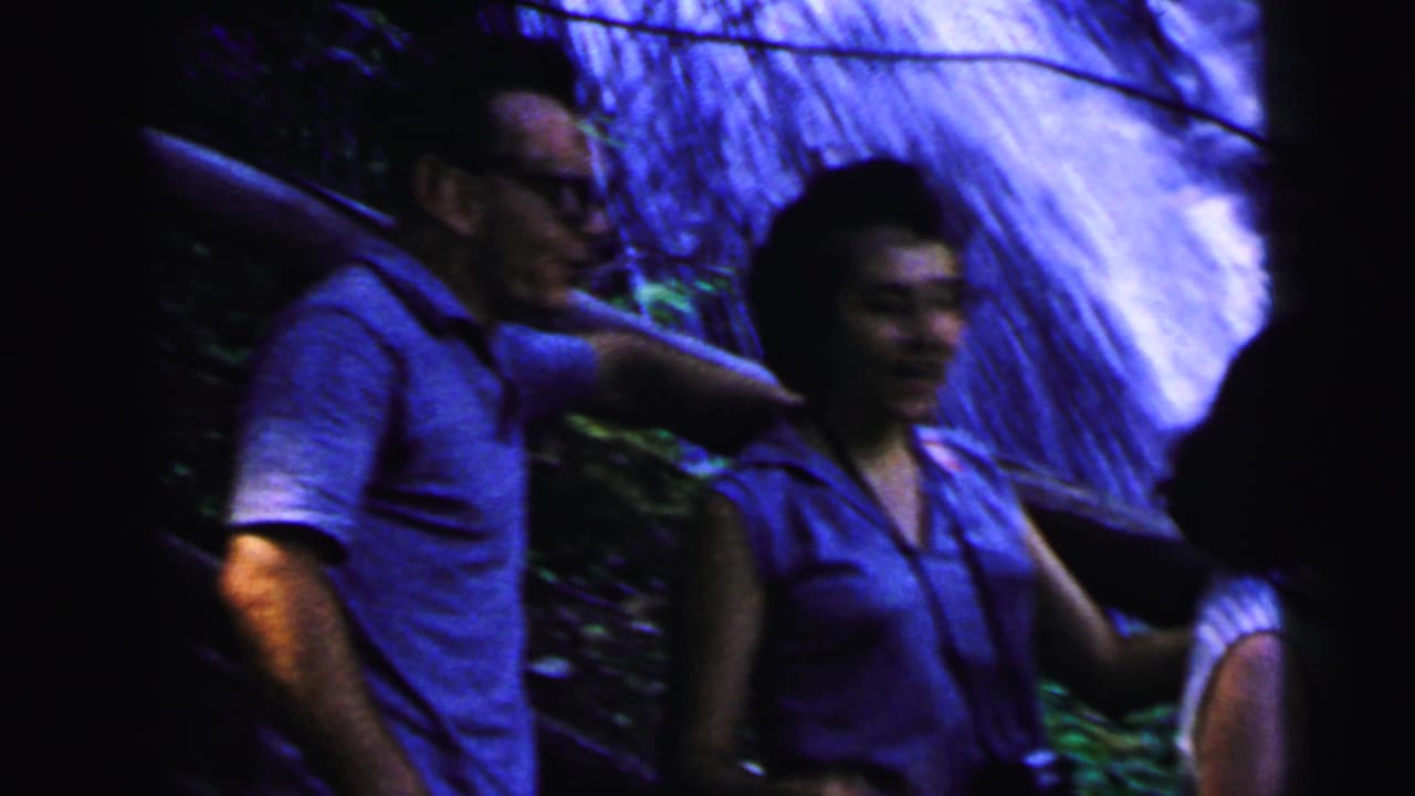 Man in glasses and blue short-sleeve shirt with companion beside a rocky waterfall, 8mm home movie circa 1964, Camden, New Jersey