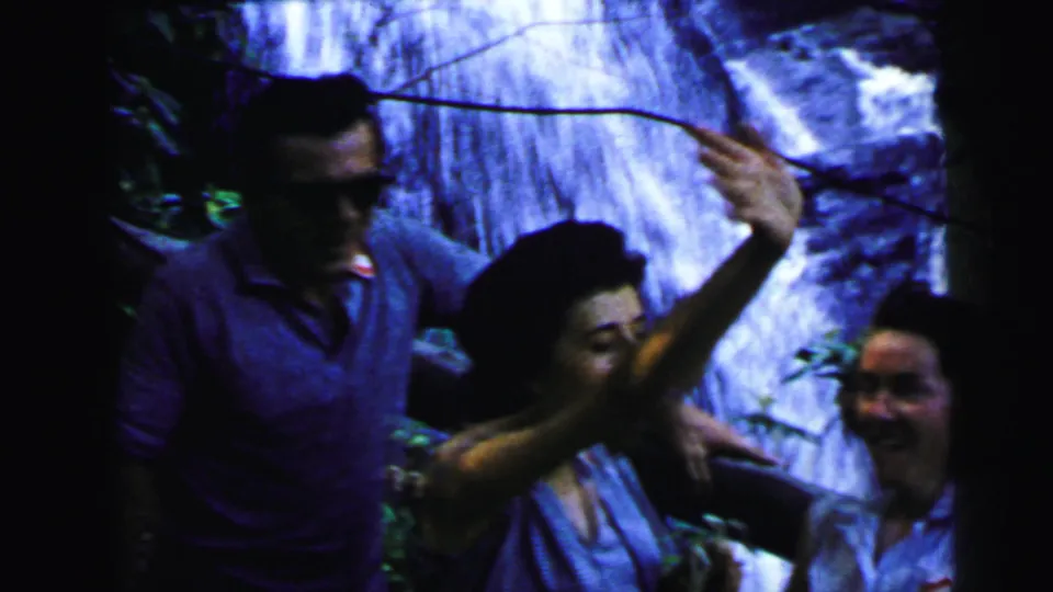 A man in sunglasses and collared shirt with two women in sleeveless blouses laughing at a cascading waterfall, 8mm home movie attributed New Jersey, 1964.
