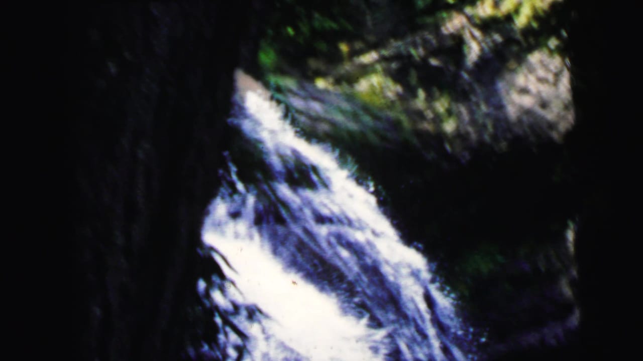 Tight shot of waterfall over mossy rocks with green foliage at frame edge; 8mm home movie, Camden New Jersey, 1964.