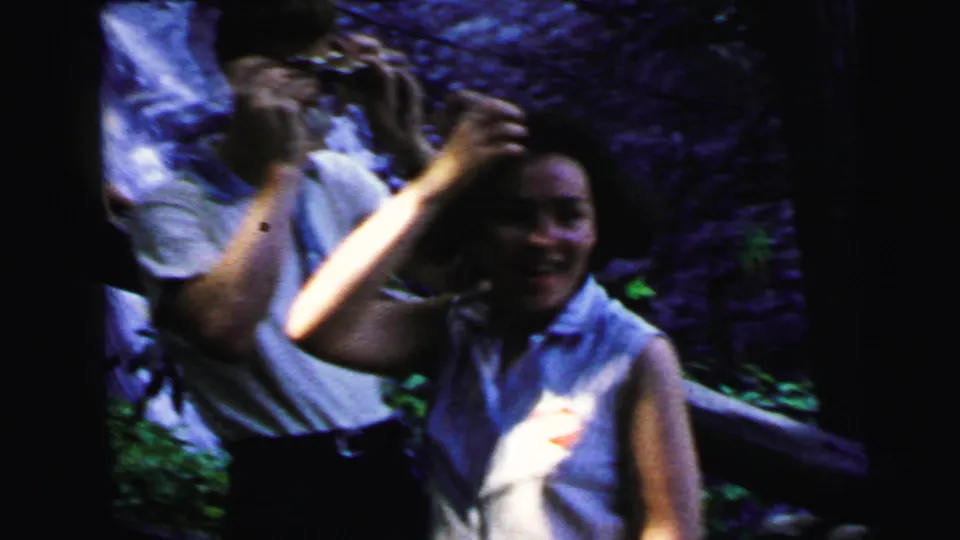 Smiling woman gesturing at waterfall, second person behind; candid 8mm home movie moment, Camden New Jersey, 1964.