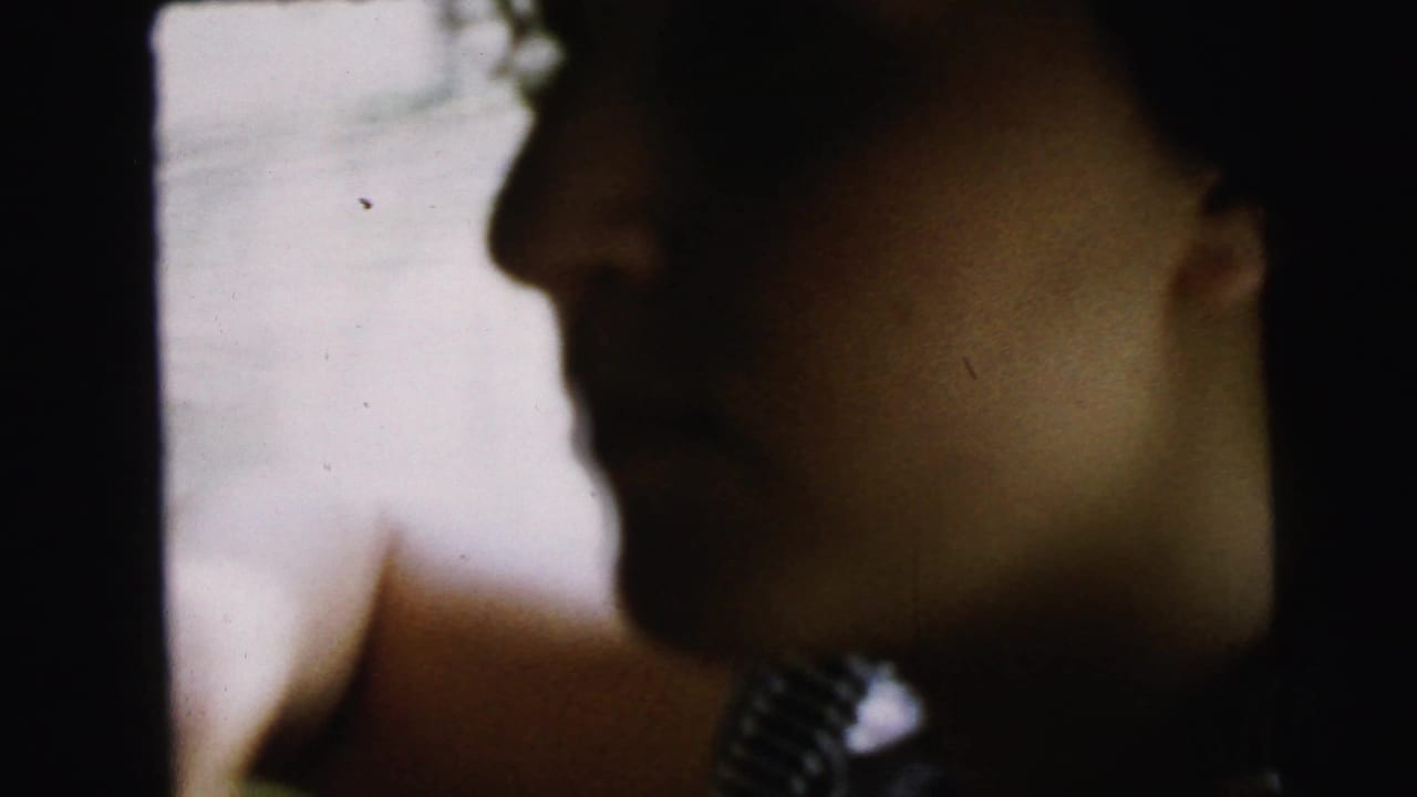 Extreme close-up of a person's face in heavy shadow, largely obscured, with visible film grain.