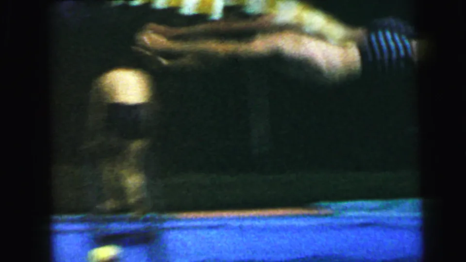Heavily motion-blurred figure in dark striped swimwear captured mid-motion at the pool edge; blue tile pool surround visible at bottom; 8mm home movie, circa 1964.